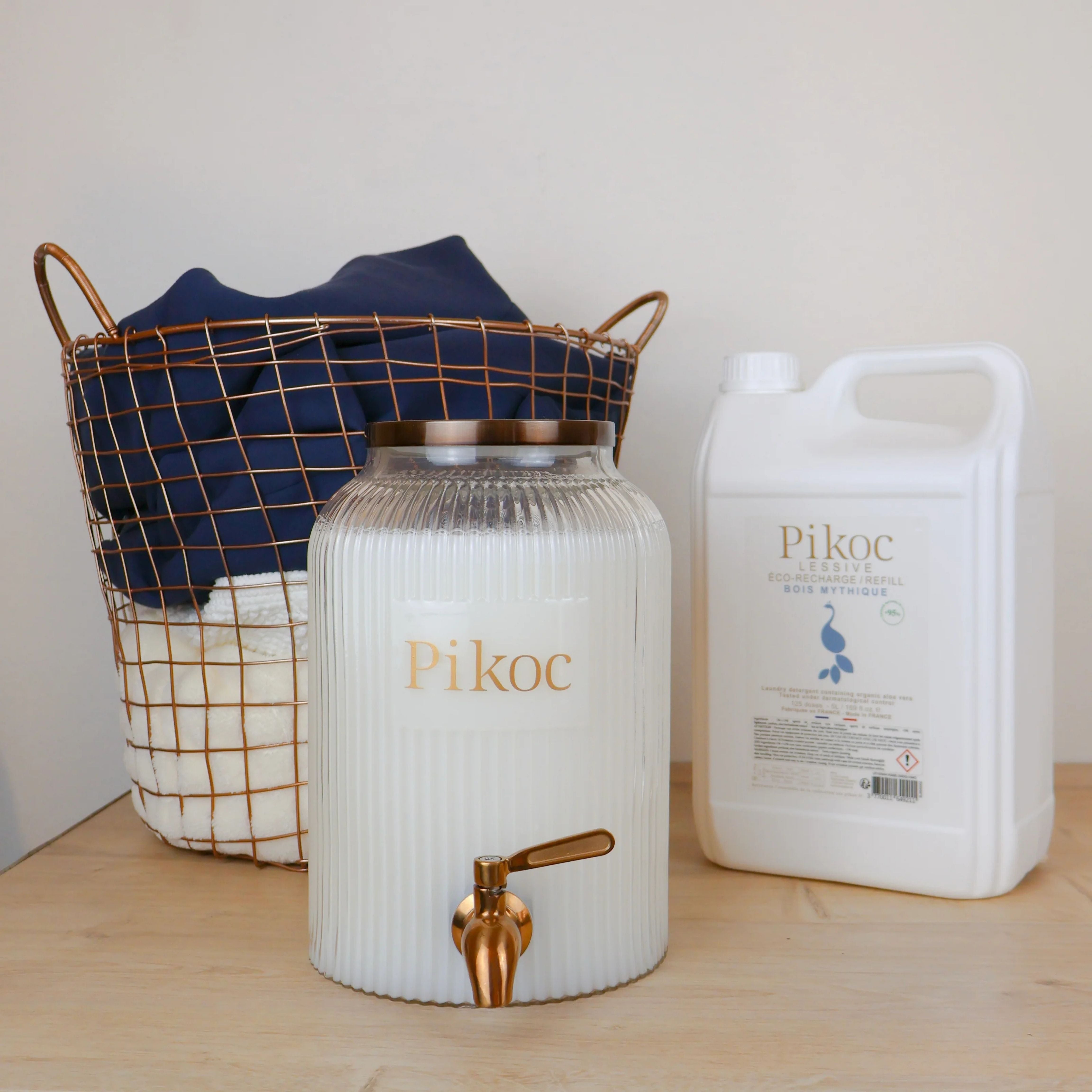 Fontaine à lessive 4L et Éco-recharge 5L Pikoc, Bois Mythique, posé sur un meuble en bois avec panier de linge