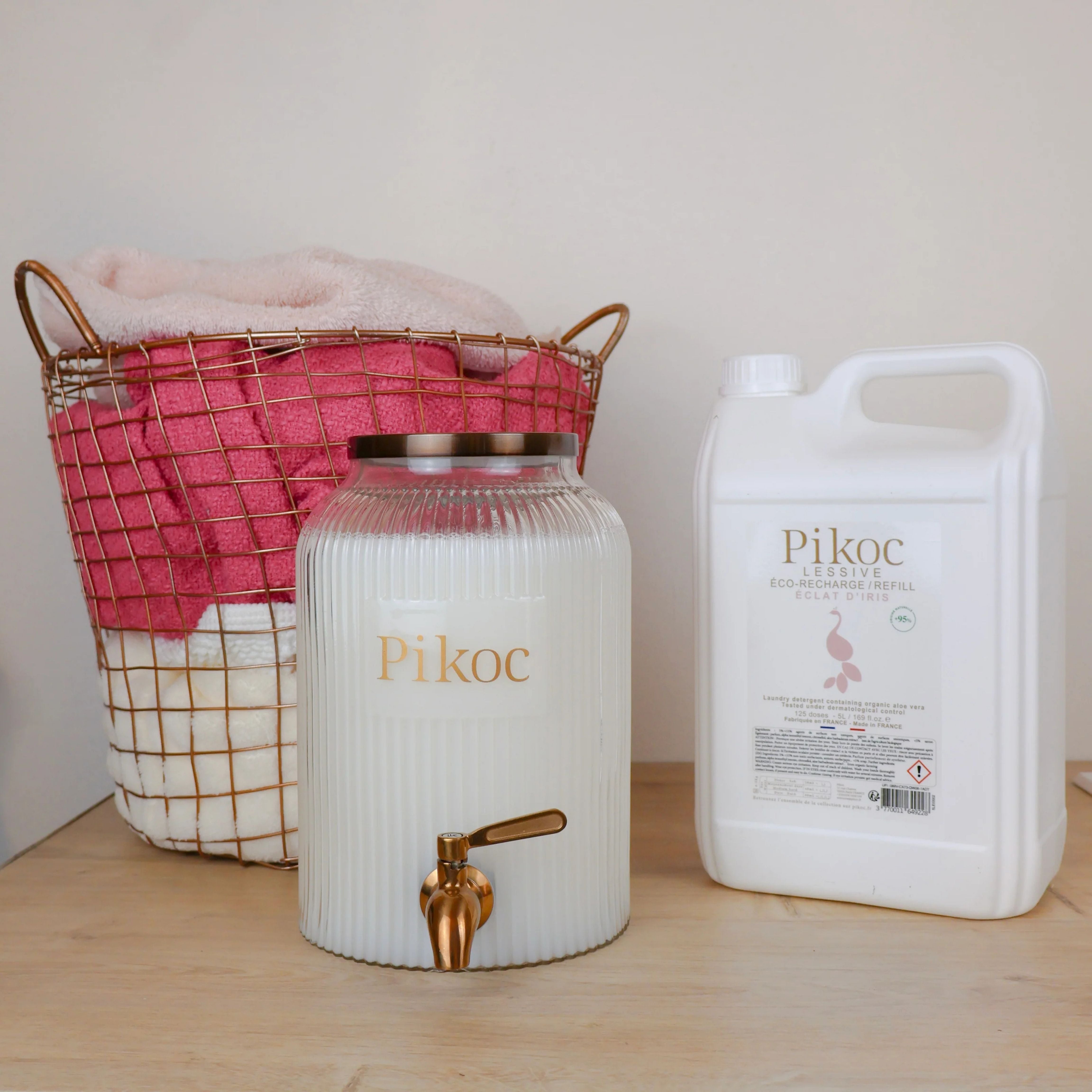 Fontaine à lessive 4L et Éco-recharge 5L Pikoc, Éclat d’Iris, posé sur un meuble en bois avec panier de linge