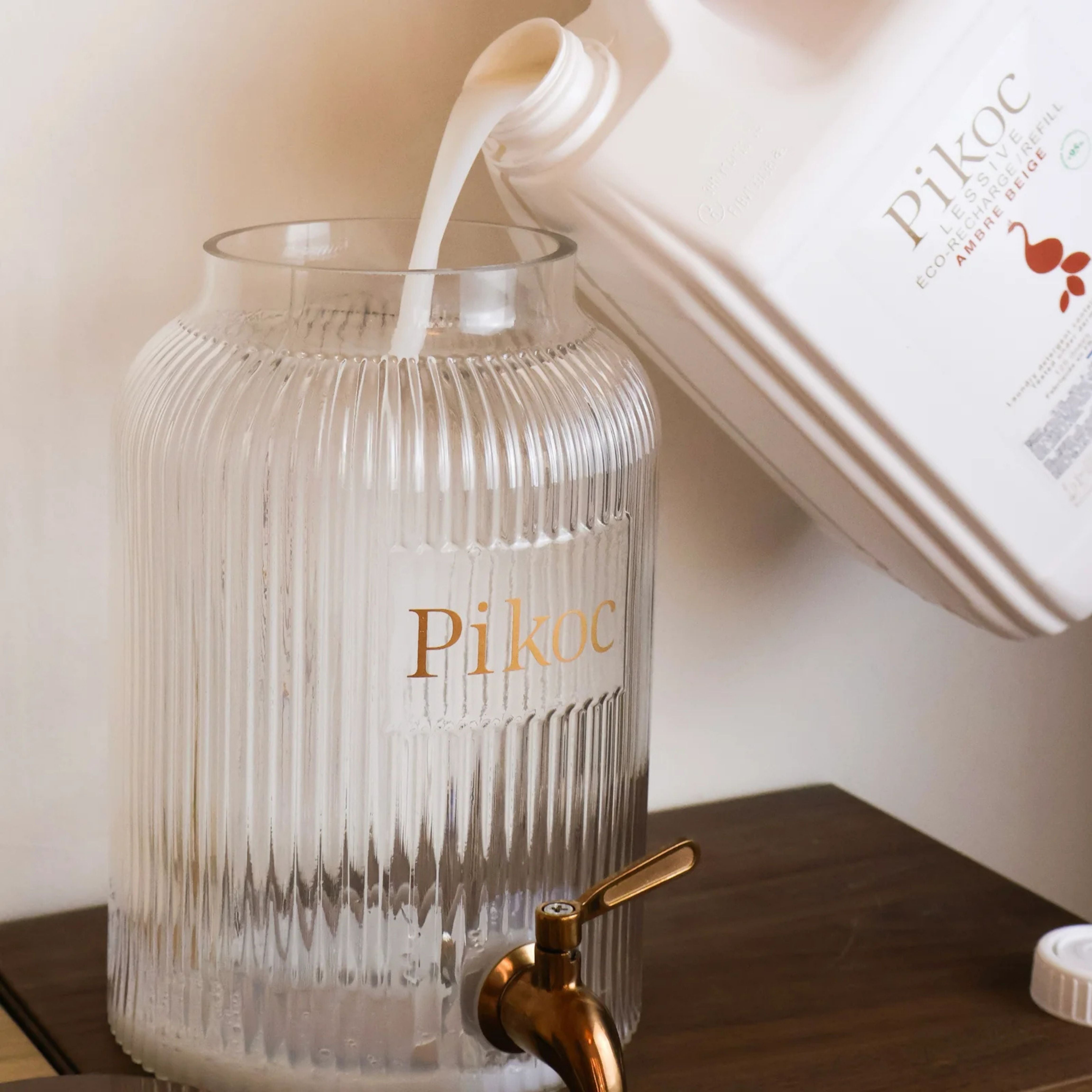Fontaine à lessive 4L Pikoc Ambre Beige, posé sur un meuble en bois en remplissage par l’Éco-recharge de 5L de lessive Ambre Beige