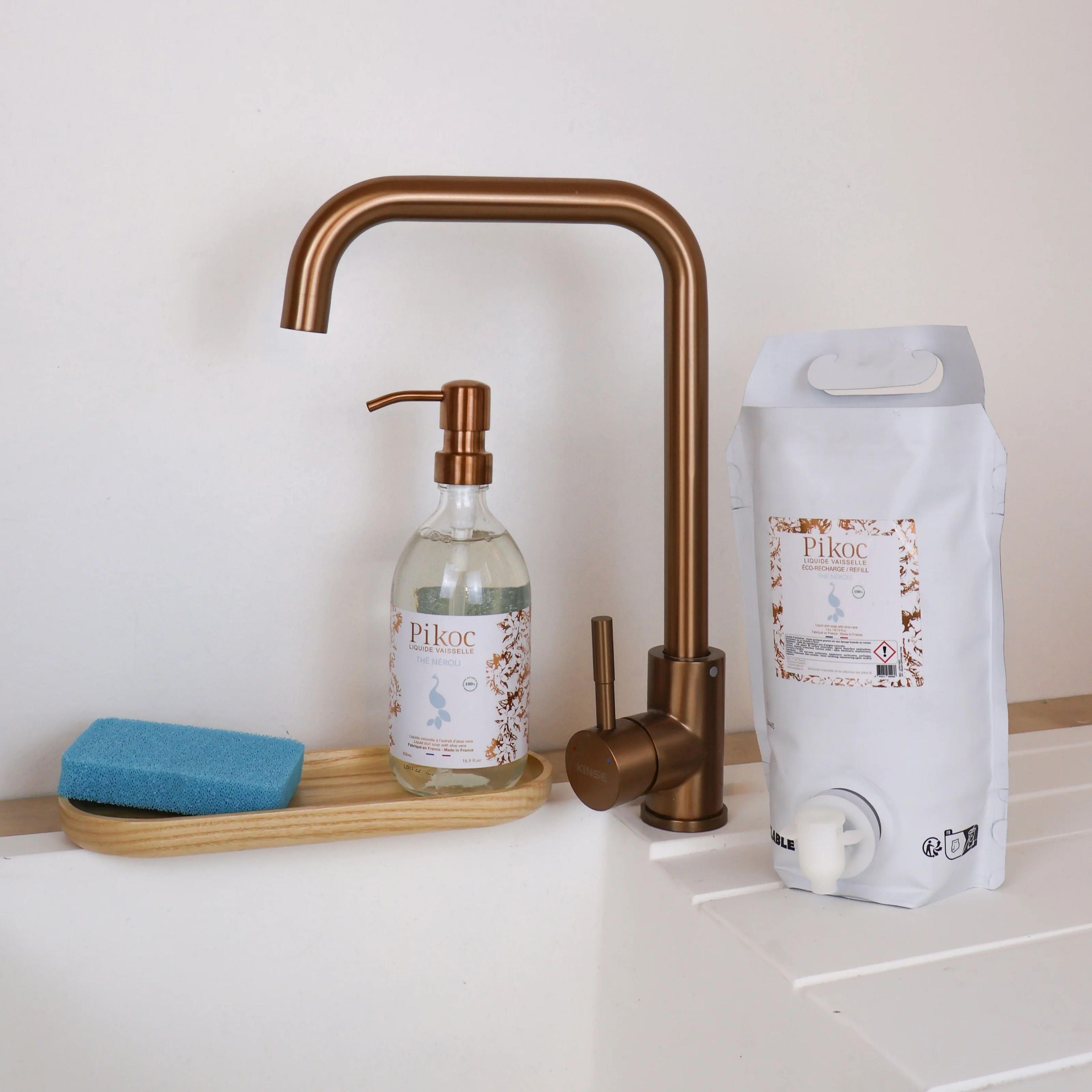 Liquide vaisselle et Eco recharge Pikoc Thé Néroli, 490mL et 1,5L, posé à côté d’un évier