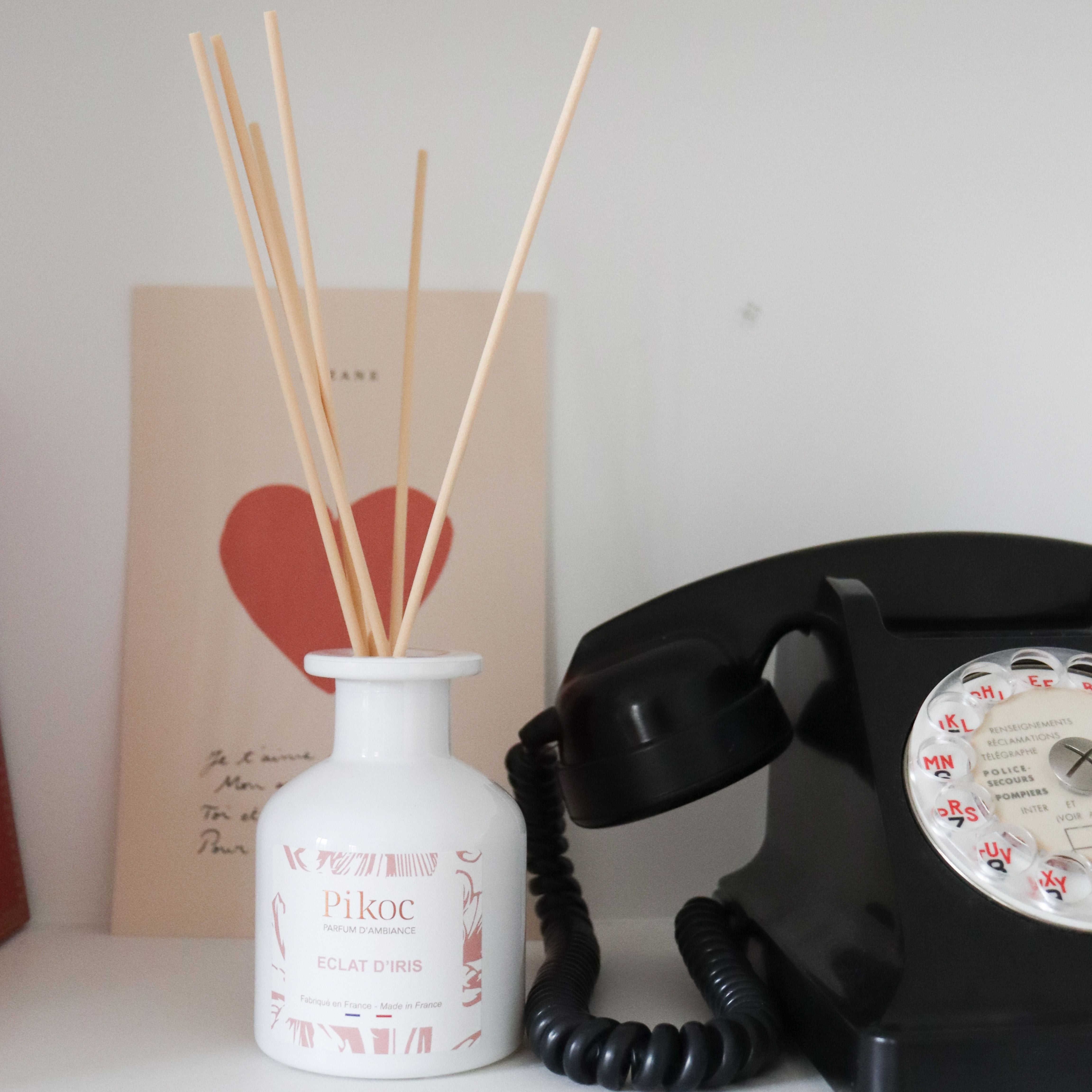 Parfum d’ambiance Pikoc Éclat d’Iris, 150mL, posé sur une étagère avec une carte et un ancien téléphone fixe